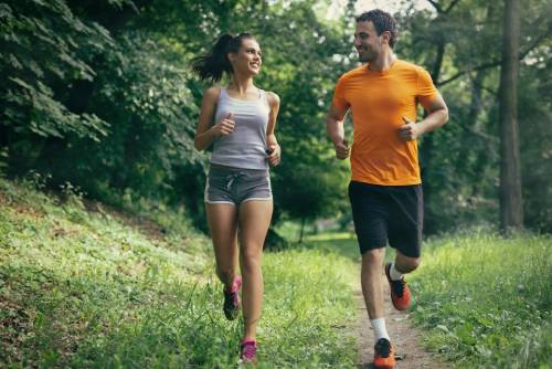 Smiling couple jogging outdoors in nature down a trail in the woods.  Fitness, sport, training, and lifestyle concept.